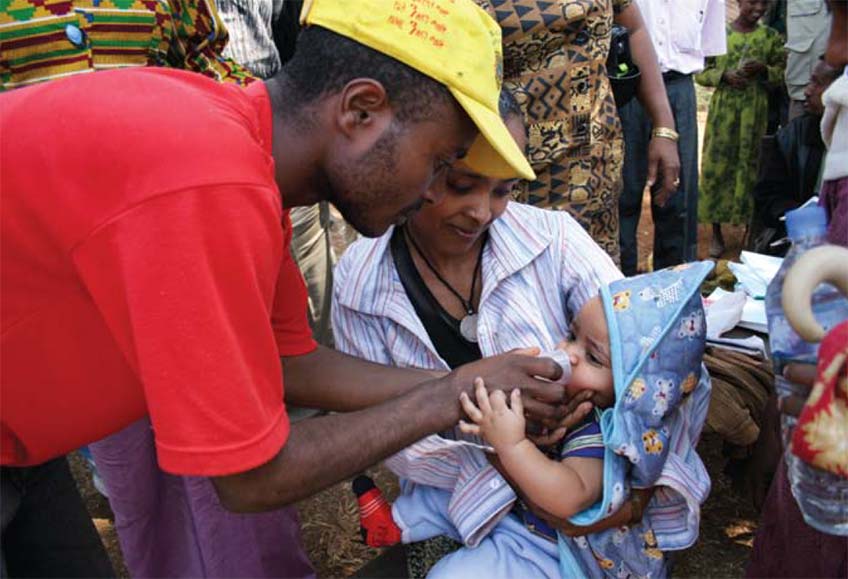A distribution worker helps a woman give her child azithromycin.
