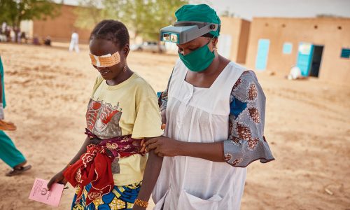 Trachoma patient with bandaged eyes escorted by a health worker.